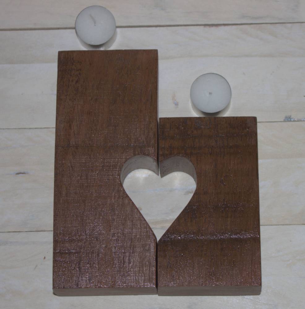 2 wooden candle holders with 1/2 heart cut out of each, paired to make a heart, laying flat in front of 2 tea light candles, sitting on a white plank table