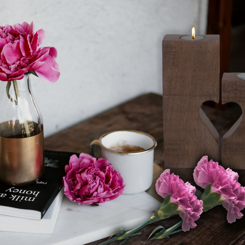 2 wooden candle holders with 1/2 heart cut in each, paired to make a heart, sitting on a table behind a cup of coffee with a book and pink flowers