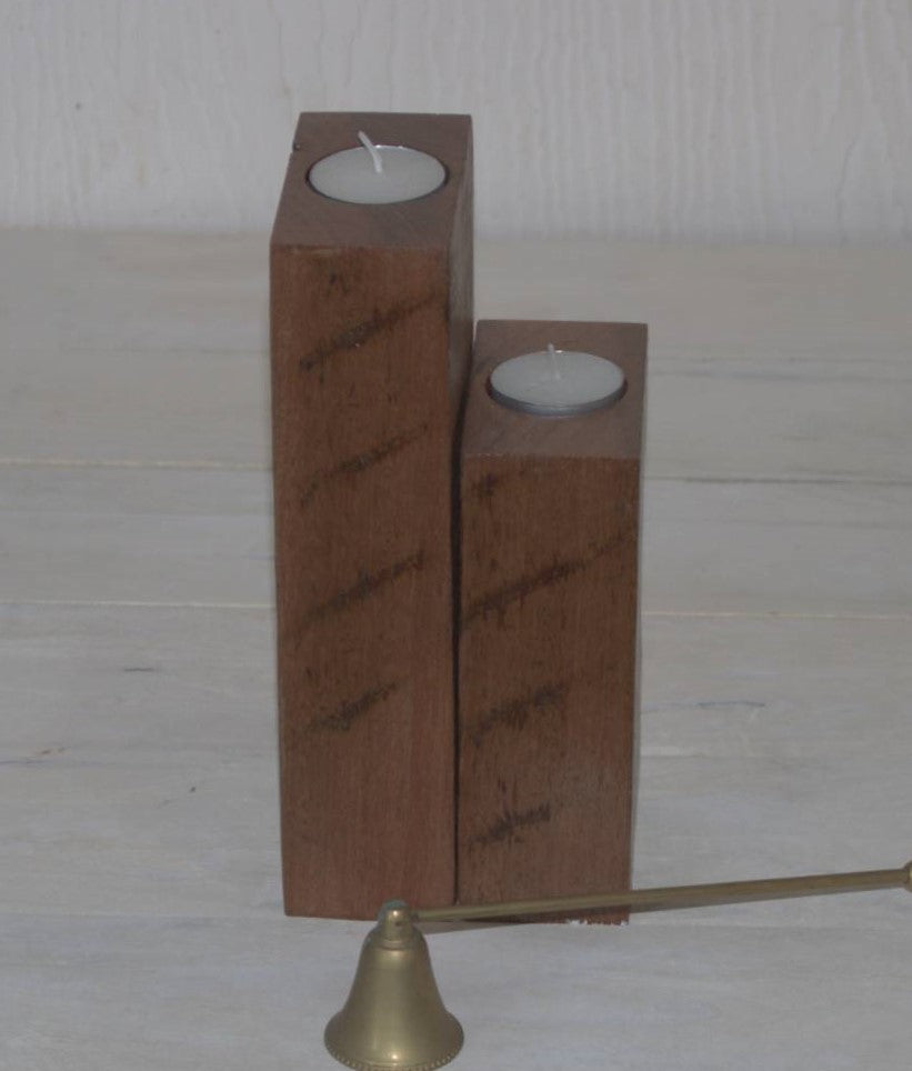 2 wooden candle holders, turned sidewards, containing tea light candles, sitting on a white plank table behind a brass candle snuffer