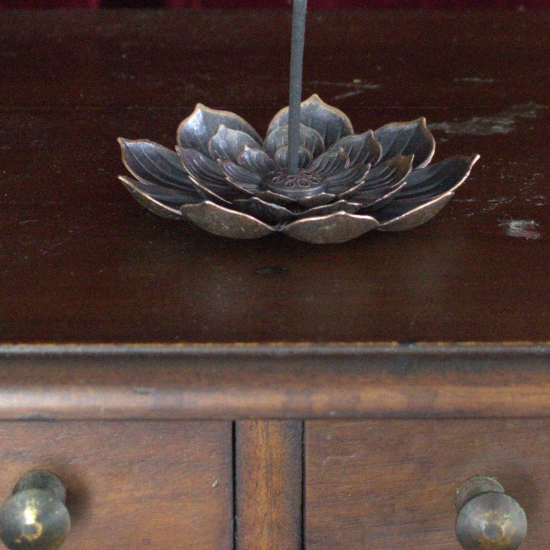 lotus flower incense holder with incense stick,  sitting on brown wooden apothecary drawers