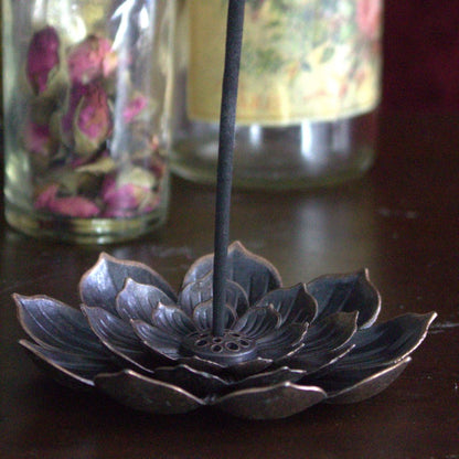 lotus flower incense holder with incense stick, sitting on  wood chest in front of floral glass bottles 