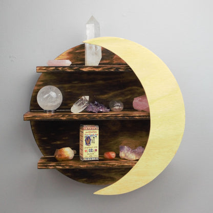 wooden crystal moon shelf with light wooden crescent moon in front of 3 shelves, holding crystals and meditation fragrance essential oil, on a grey wall