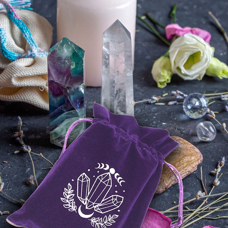 purple tarot bag with white moon and crystal print on a table with lavender sprigs, fluorite and  quartz crystal single terminated crystal