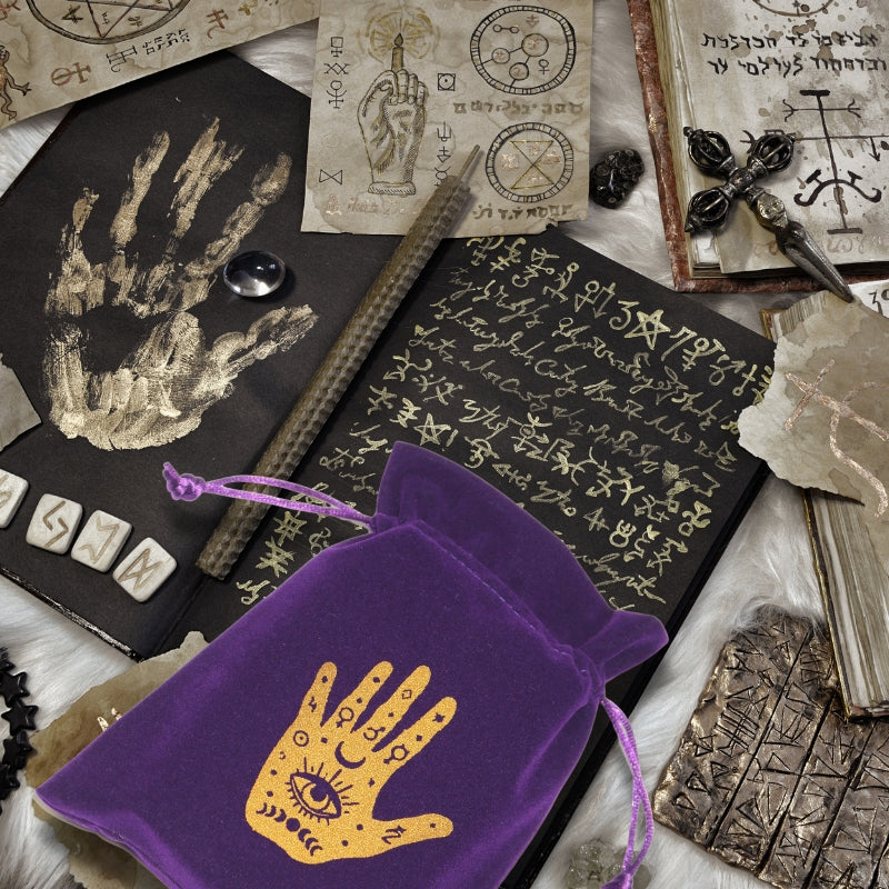purple and gold tarot bag on table with  pages of  book parchment  decorated in gold symbols 