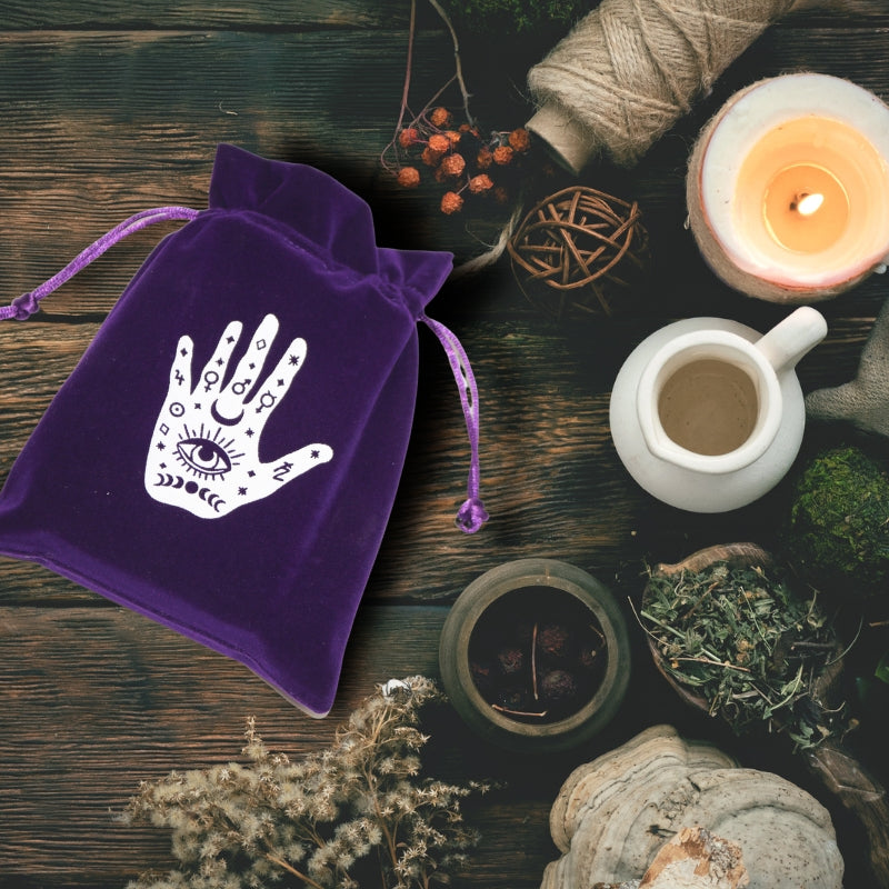 purple tarot pouch with white palm print on table with herbs, candles and a roll of natural twine