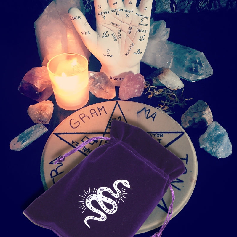 purple tarot bag sitting on a board, in front of a candle and palm statue, surrounded by crystals