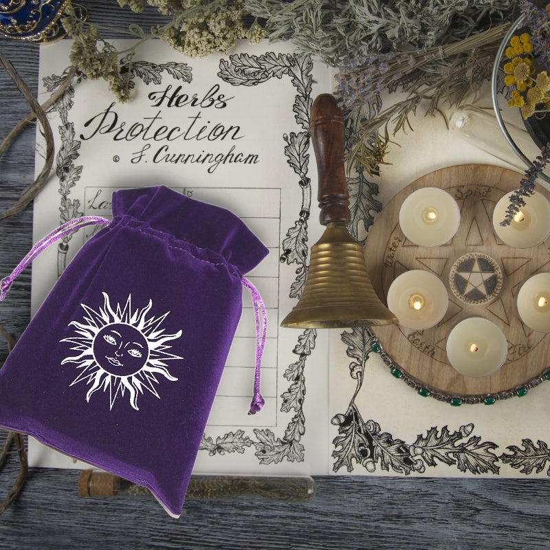 purple tarot bag on a nature witches diary next to a pentagram board with 5 candles and a bell, surrounded by herbs