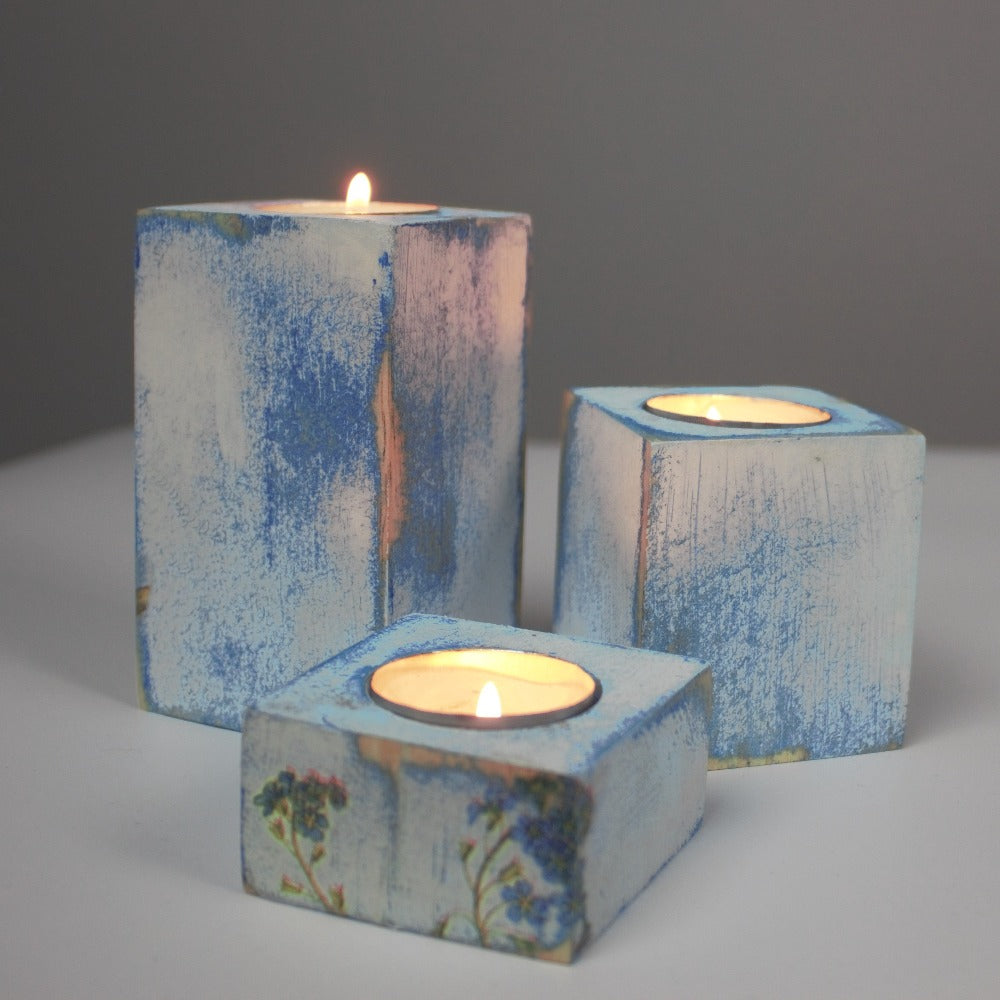 blue and white distressed set of 3 candle holders with lit tea light candles, decorated with blue flowers