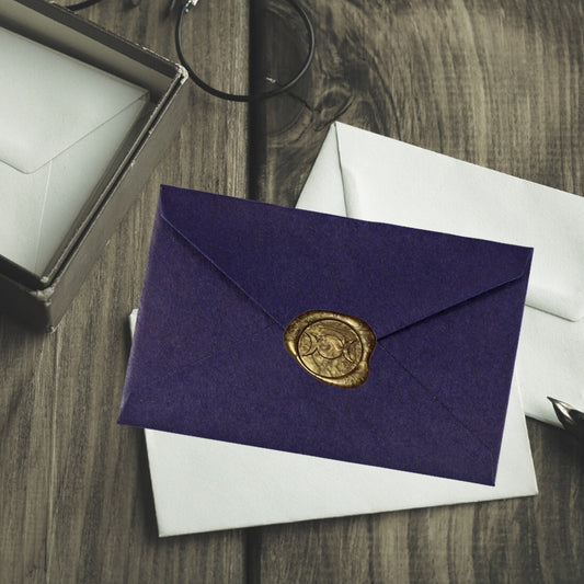 gold triple moon wax seal on a purple envelope, sitting on a wooden table with white envelopes 