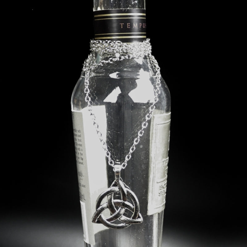 silver coloured triquetra necklace hanging on a bottle with a black background