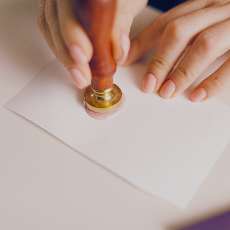 person using a brass wax seal stamp to stamp paper