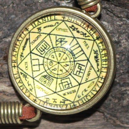 Glass cabochon featuring a yellow and black image of the seals of the seven archangels in a gold coloured ring attached to a leather strap, adjustable by way of clasp and chain link