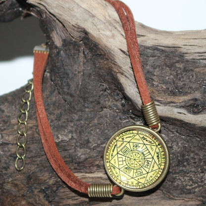 Glass cabochon featuring a yellow and black image of the seals of the seven archangels in a gold coloured ring attached to a leather strap, adjustable by way of clasp and chain link